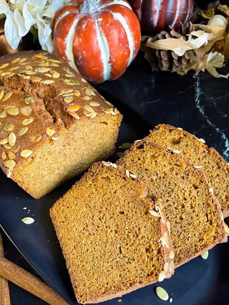 Baked pumpkin bread, sliced, on a dark platter.