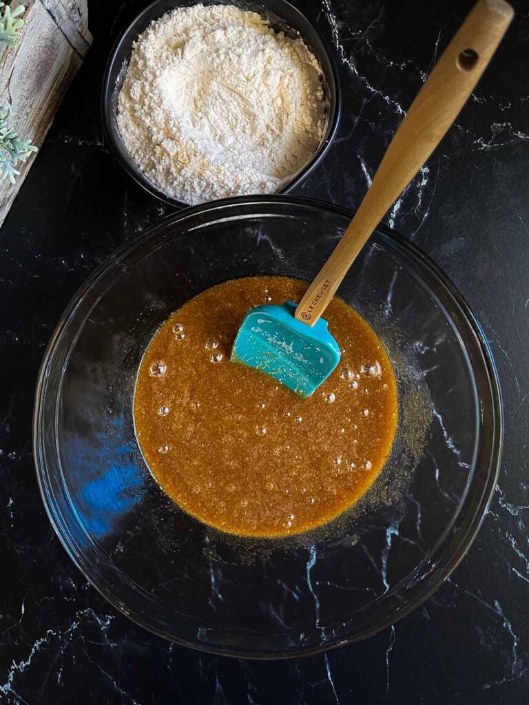 Mixing salted butterscotch pretzel cookie dough ingredients in a glass bowl on a dark surface.