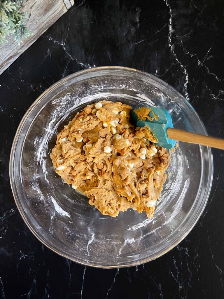 Salted Butterscotch Pretzel Cookie dough in a glass bowl on a dark surface.