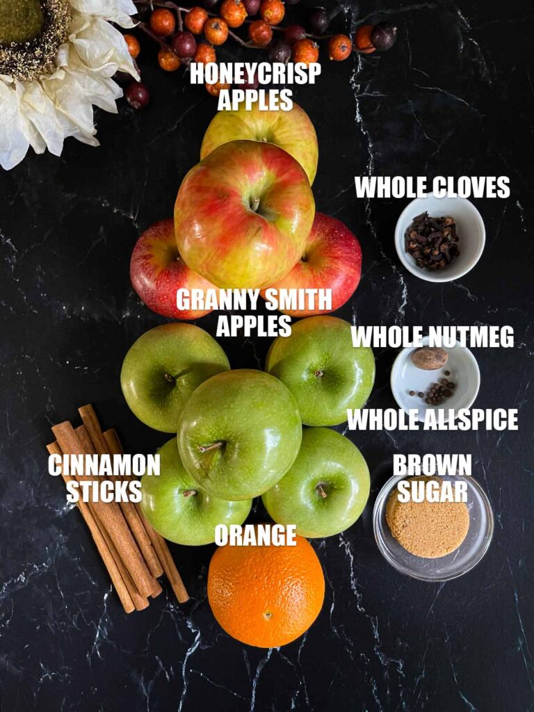 Ingredients for slow cooker apple cider on a dark surface.