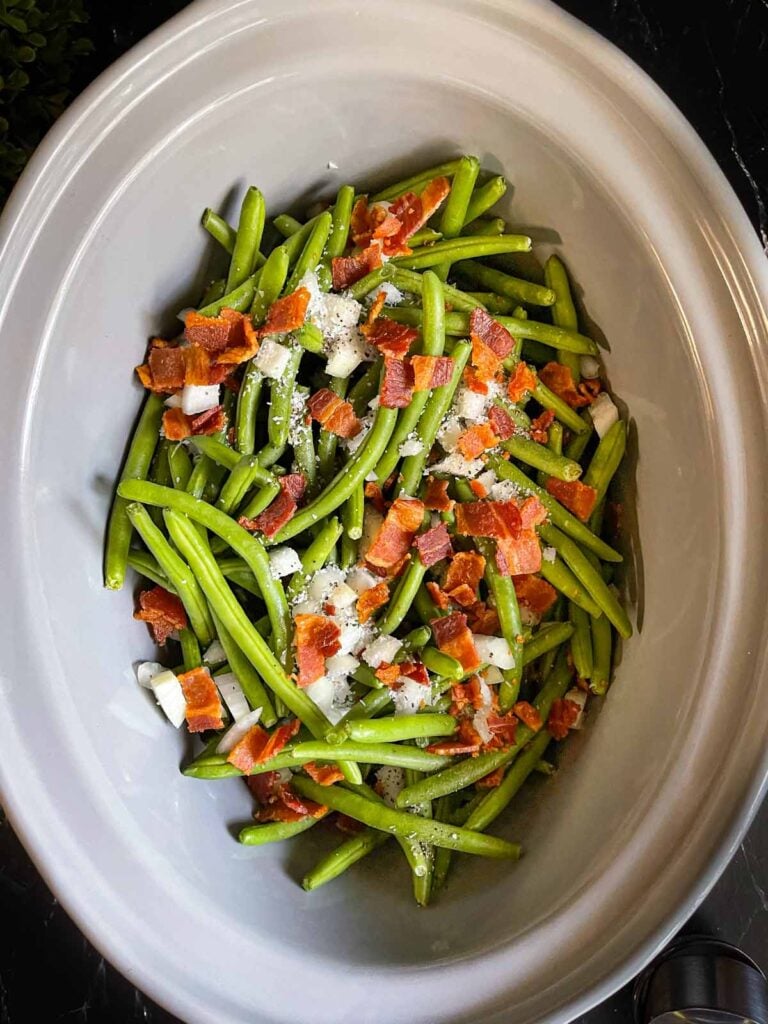 Raw green beans with onions and bacon in a slow cooker.