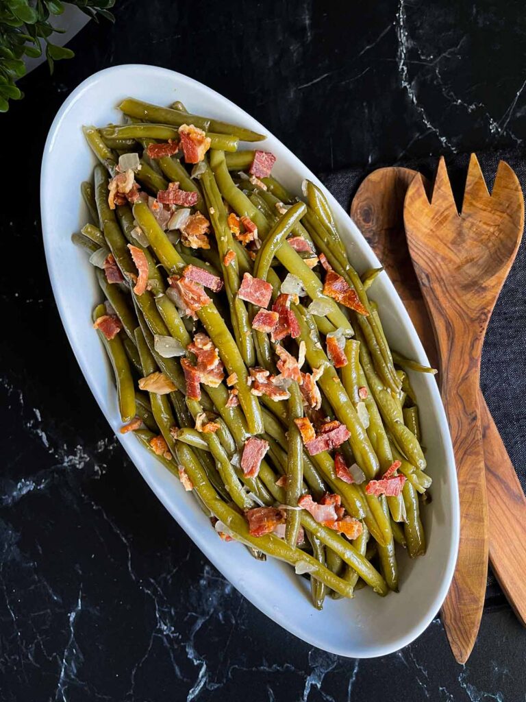 Slow cooker green beans in a white serving bowl on a dark surface.