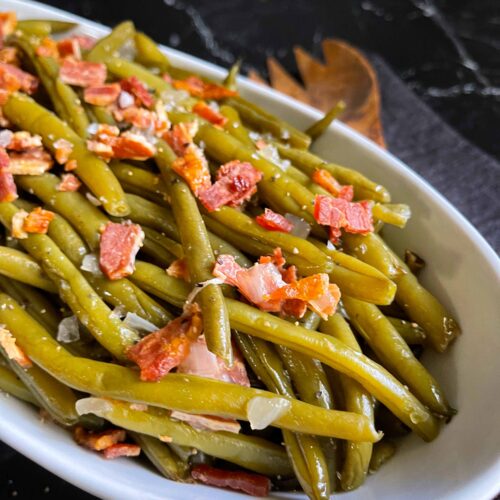 Slow cooker green beans in a white serving bowl on a dark surface.