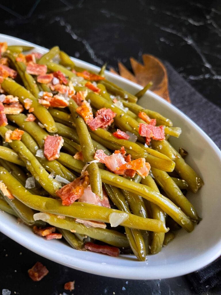 Slow cooker green beans in a white serving bowl on a dark surface.