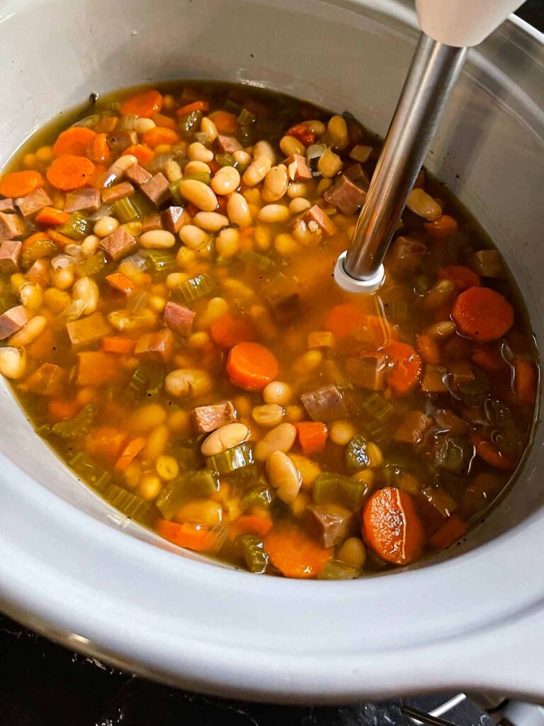 Immersion blender being used on ham and bean soup to make it thicker.