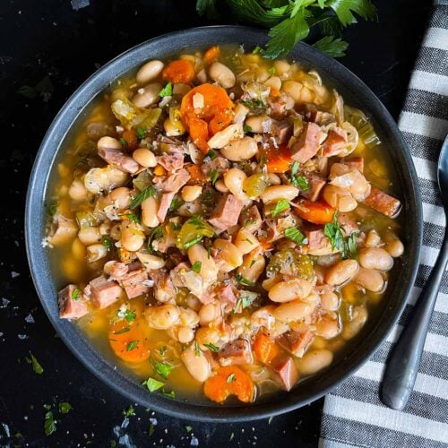 Ham and bean soup in a dark bowl on a dark surface.