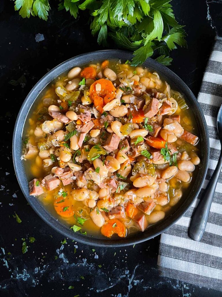 Ham and bean soup in a dark bowl on a dark surface.