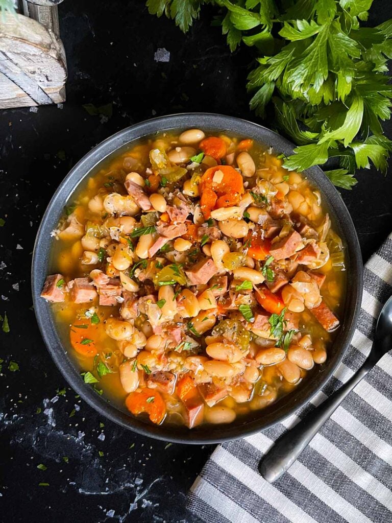 Ham and bean soup in a dark bowl on a dark surface.