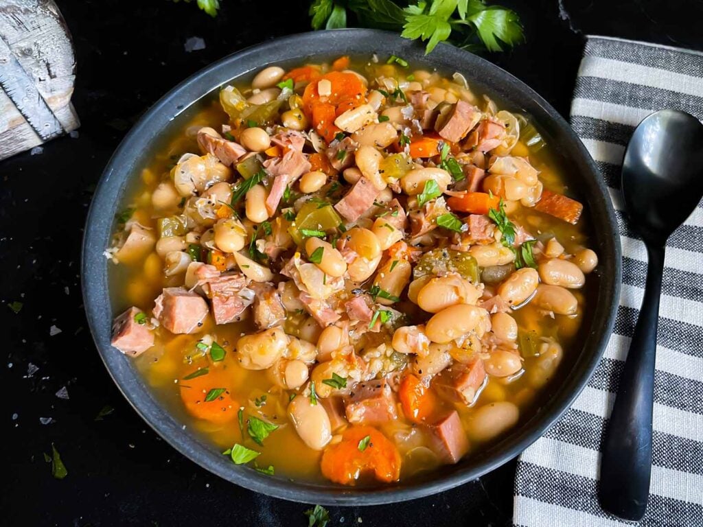 Ham and bean soup in a dark bowl on a dark surface.