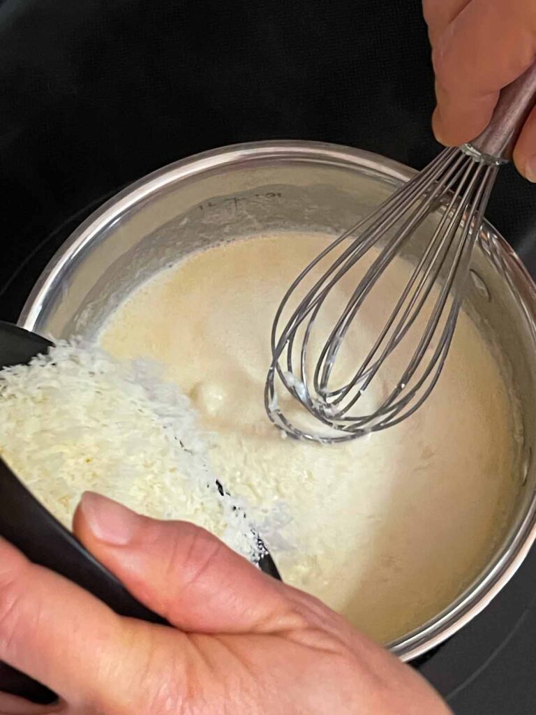 Adding parmesan cheese to the sauce for slow cooker Tuscan chicken.