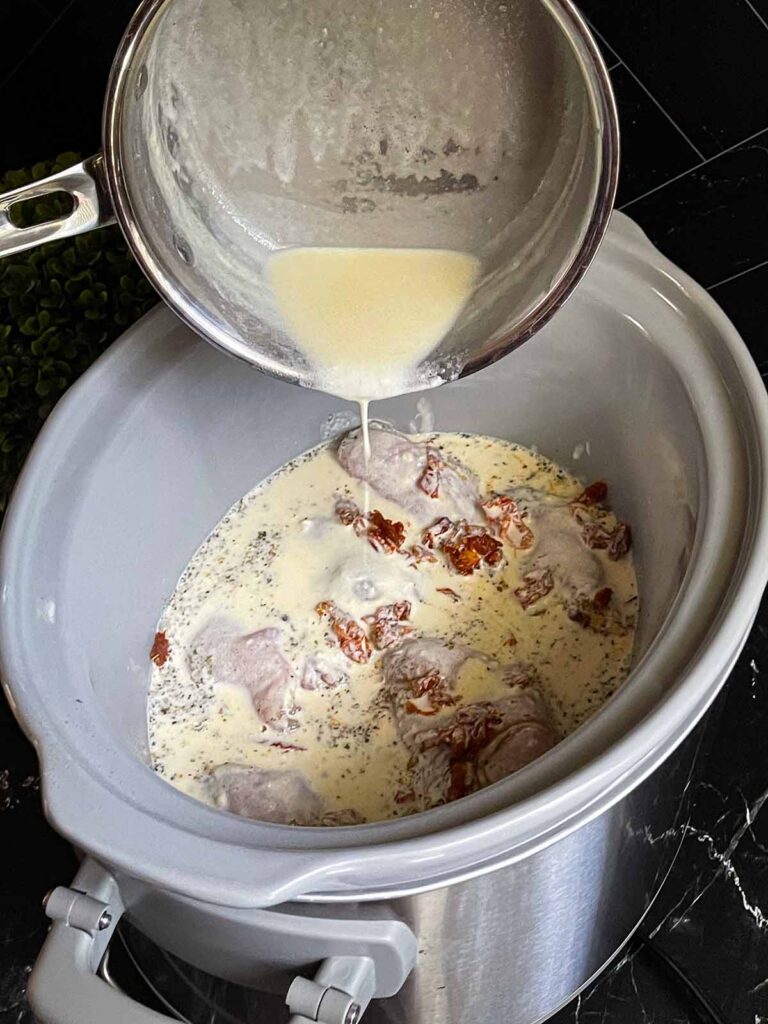 Pouring the Tuscan chicken sauce over raw chicken in a slow cooker.