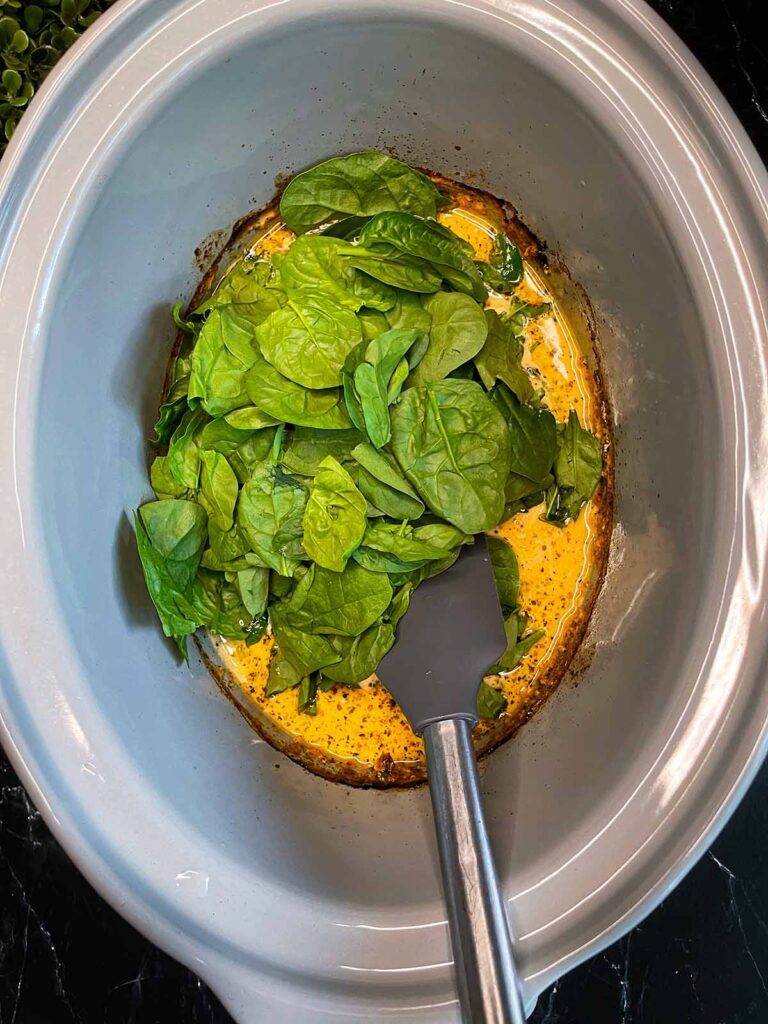 Adding spinach to the Tuscan chicken in a slow cooker.