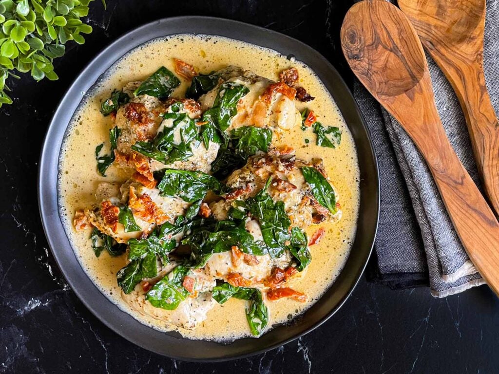 Slow Cooker Tuscan Chicken in a dark bowl on a dark surface.