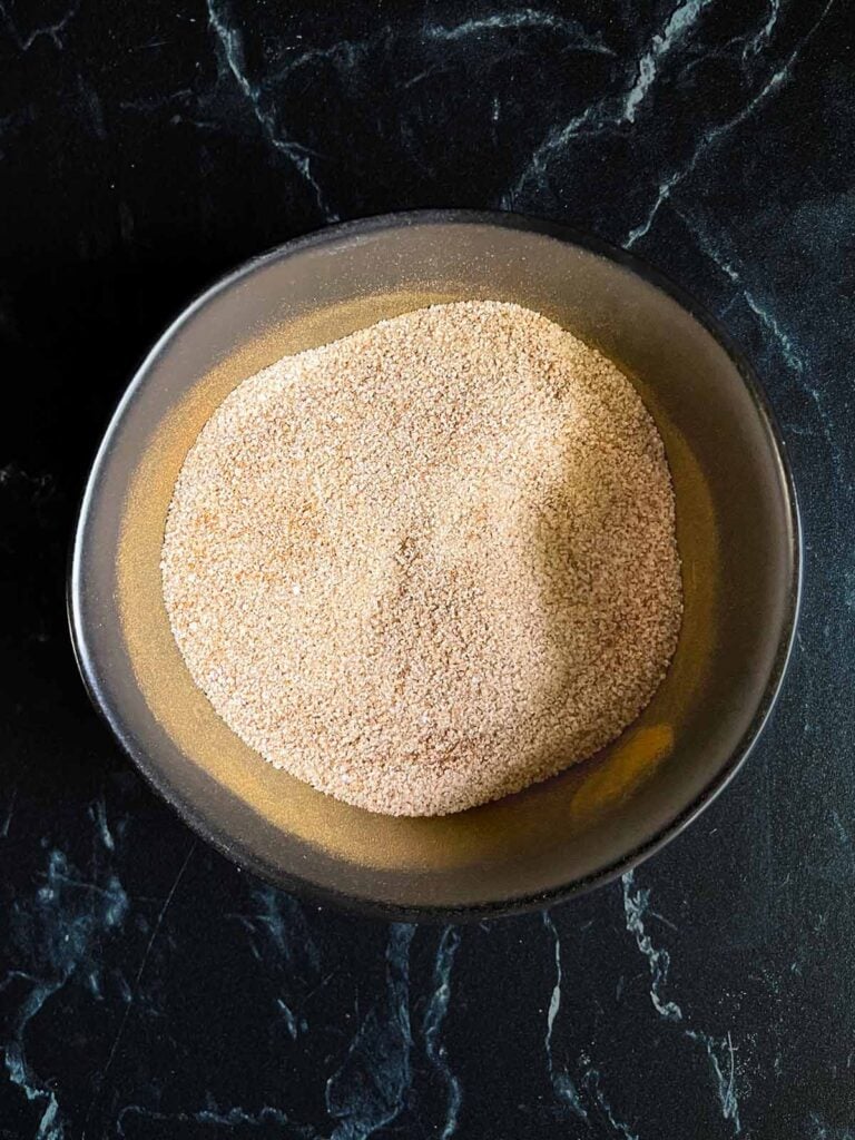 Cinnamon sugar mixture for Snickerdoodle Bars in a small bowl on a dark surface.