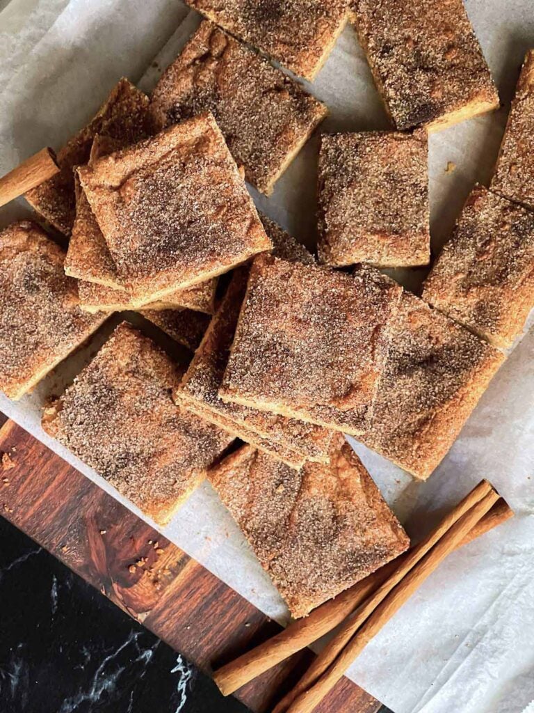 Snickerdoodle Bars stacked on a wooden cutting board.