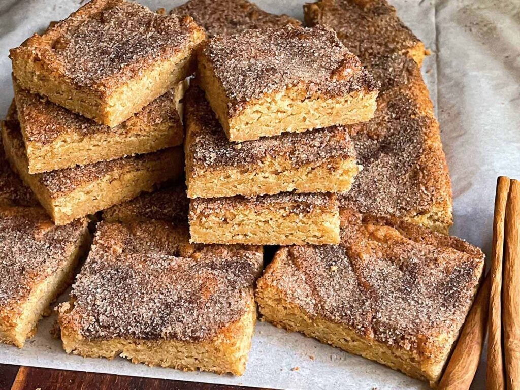 Snickerdoodle Bars stacked on a wooden cutting board.