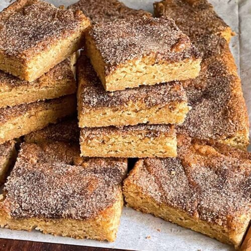 Snickerdoodle Bars stacked on a wooden cutting board.