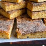 Snickerdoodle Bars stacked on a wooden cutting board.