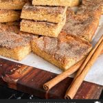 Snickerdoodle Bars stacked on a wooden cutting board.