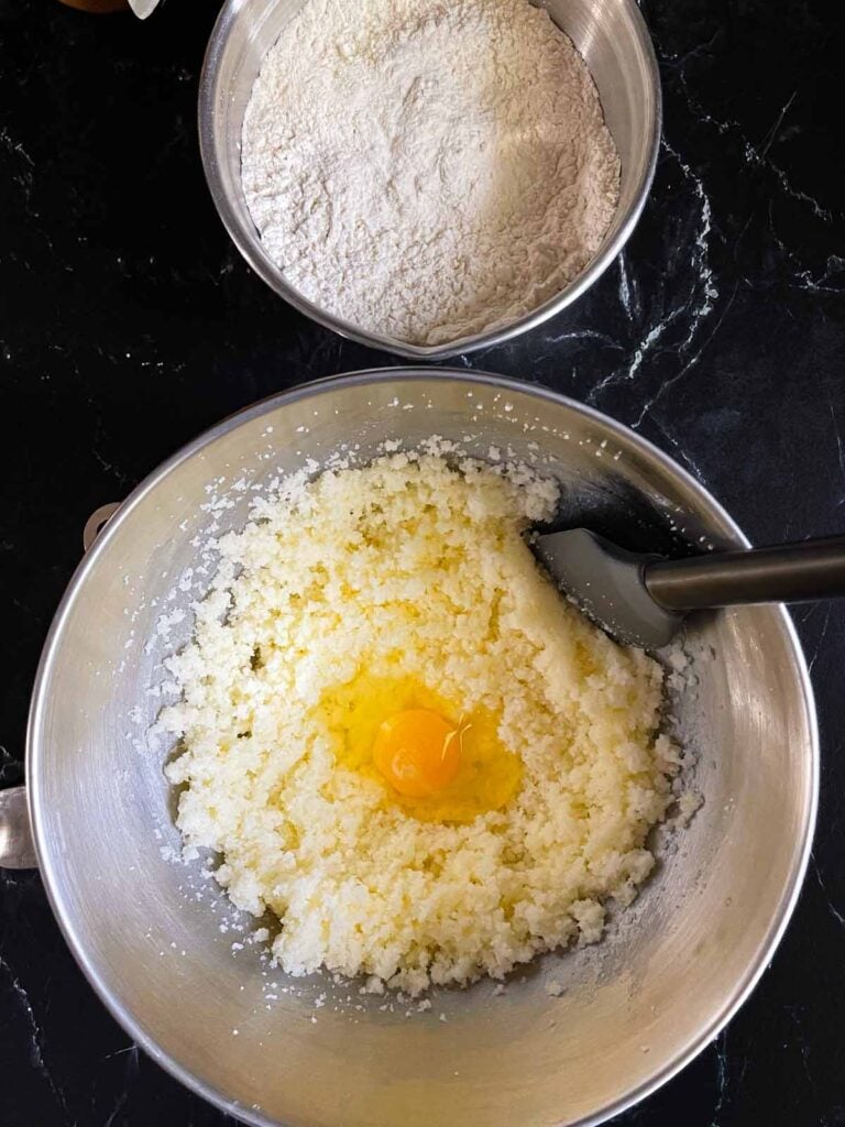 Eggs being added to one at a time to the creamed butter and sugar in a metal mixing bowl.