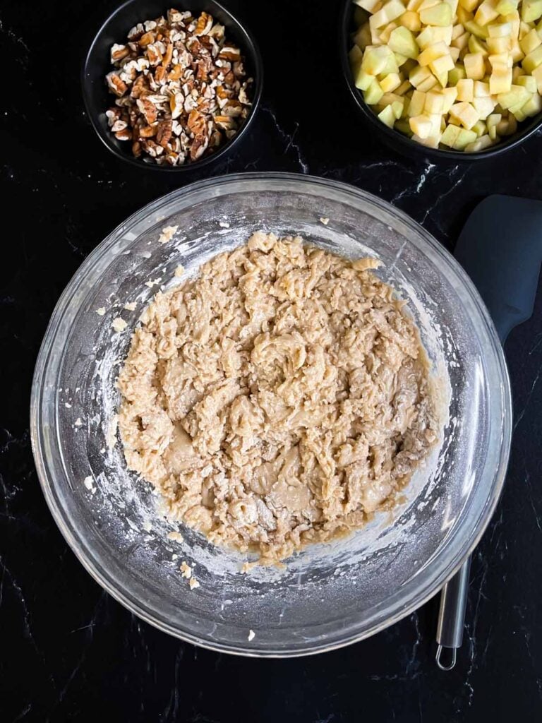 Dry ingredients mixed into the wet ingredients for apple dapple cake in a glass bowl on dark surface.