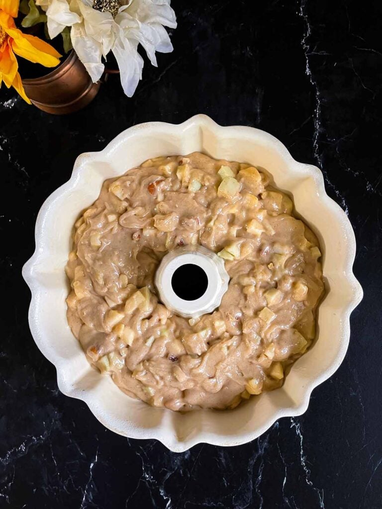 Unbaked apple bundt cake batter in a bundt pan on a dark surface.