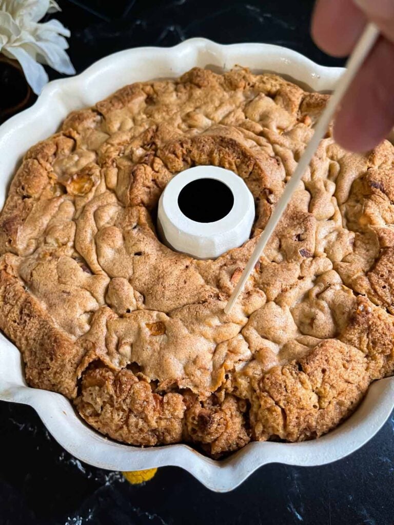 Holes being poked into the baked apple dapple cake in a bundt pan on a dark surface.