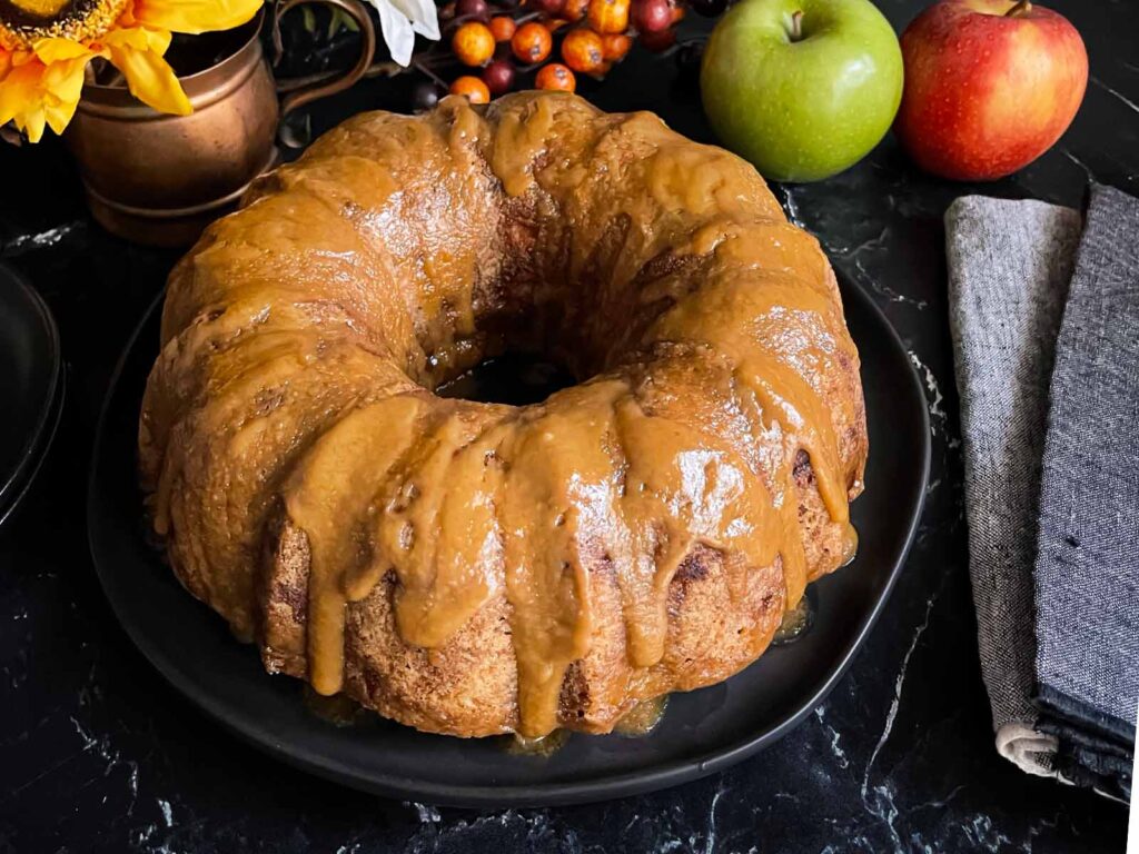 Caramel glazed apple dapple cake on a dark plate on a dark surface.