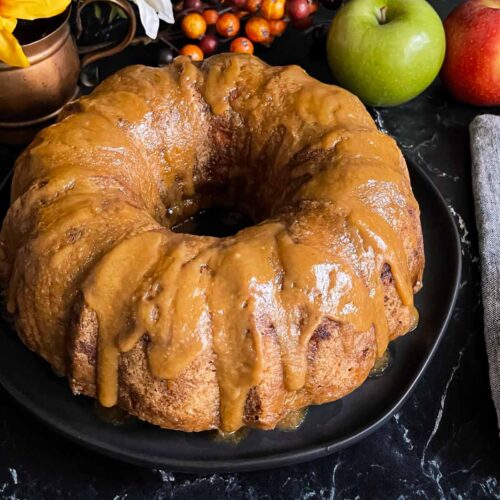 Caramel glazed apple dapple cake on a dark plate on a dark surface.