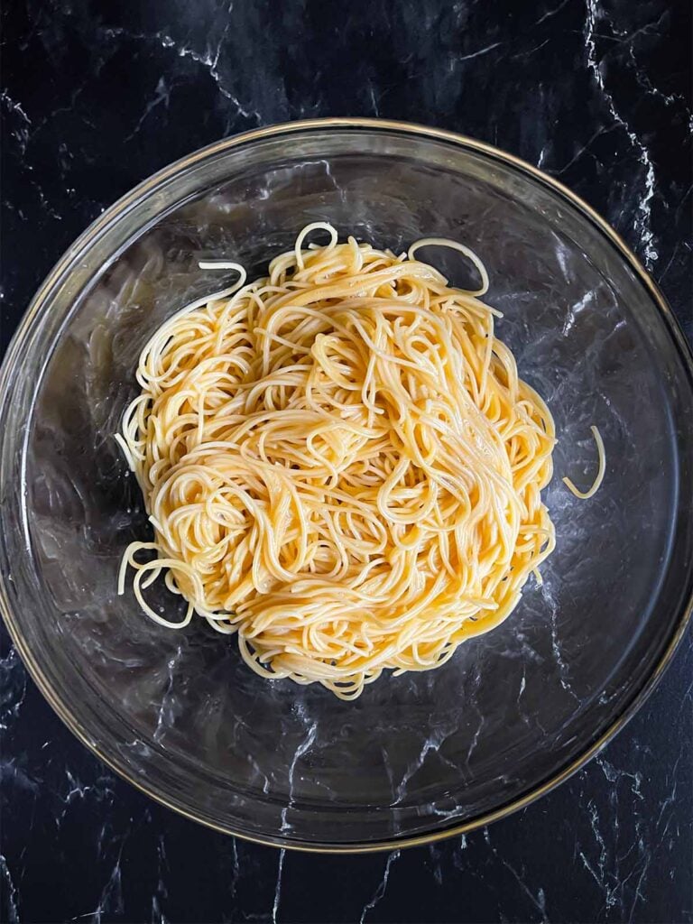 Cooled spaghetti tossed with the beaten eggs for baked spaghetti in a glass mixing bowl.