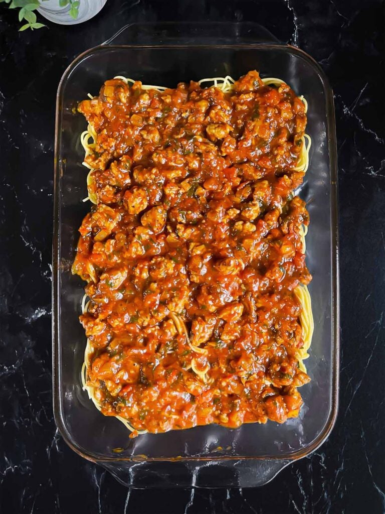 Layer of marinara sauce over the spaghetti in a glass baking pan.