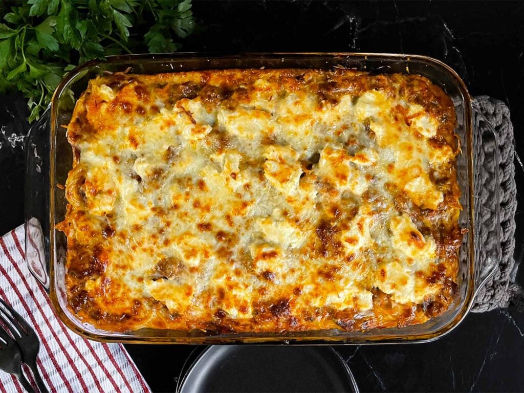 Baked spaghetti in a glass baking dish on a dark surface.