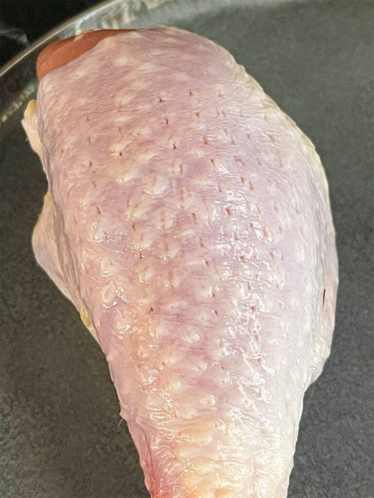 A chicken leg showing that the skin has been pierced with a meat tenderizer.