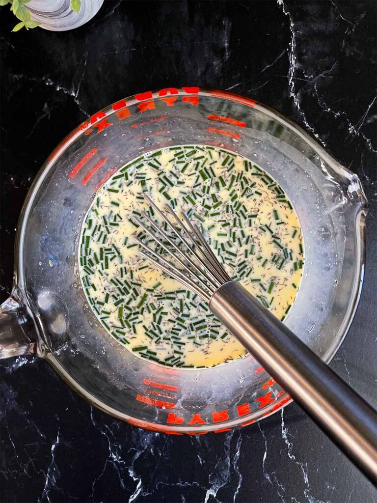 Ham and cheese strata egg mixture in a large glass measuring bowl.