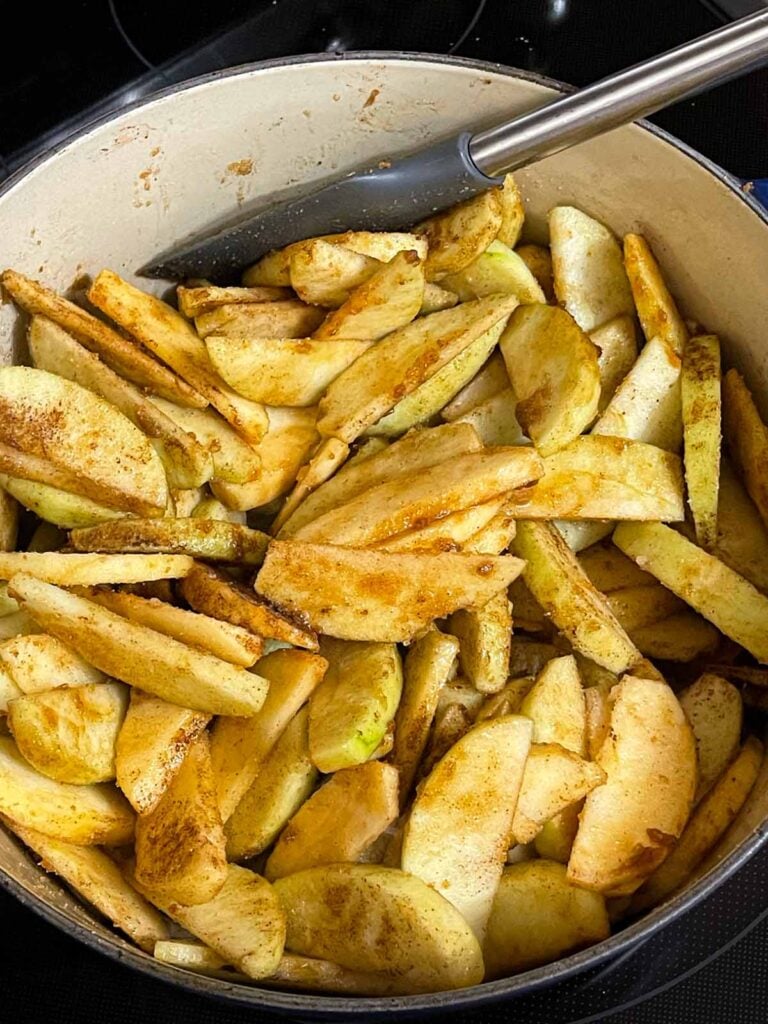 Slices apples tossed with sugar and spices for apple pie in a large dutch oven.