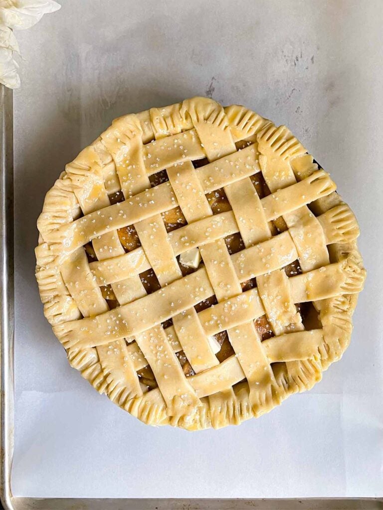 Unbaked lattice crust apple pie on a parchment paper lined baking sheet.