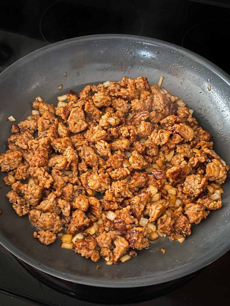 Browned italian sausage with translucent onions in a skillet.