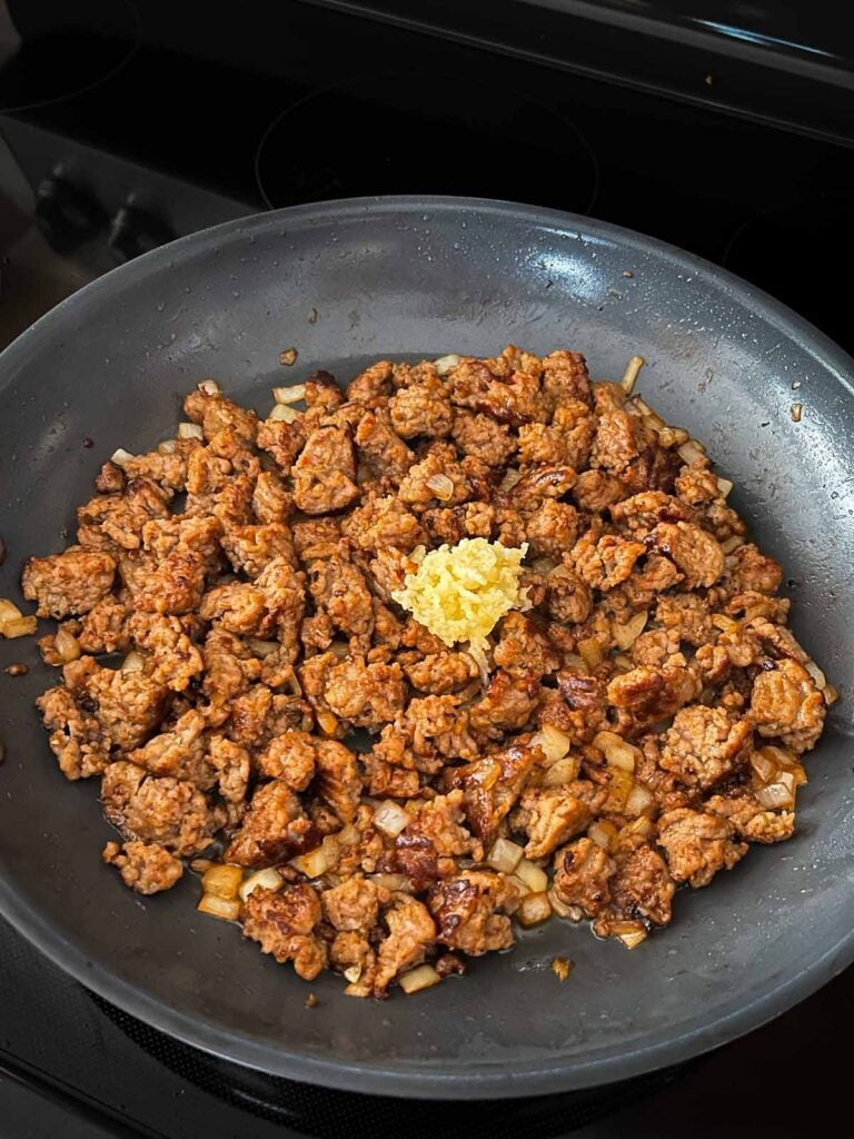 Garlic added to browned italian sausage in a skillet.
