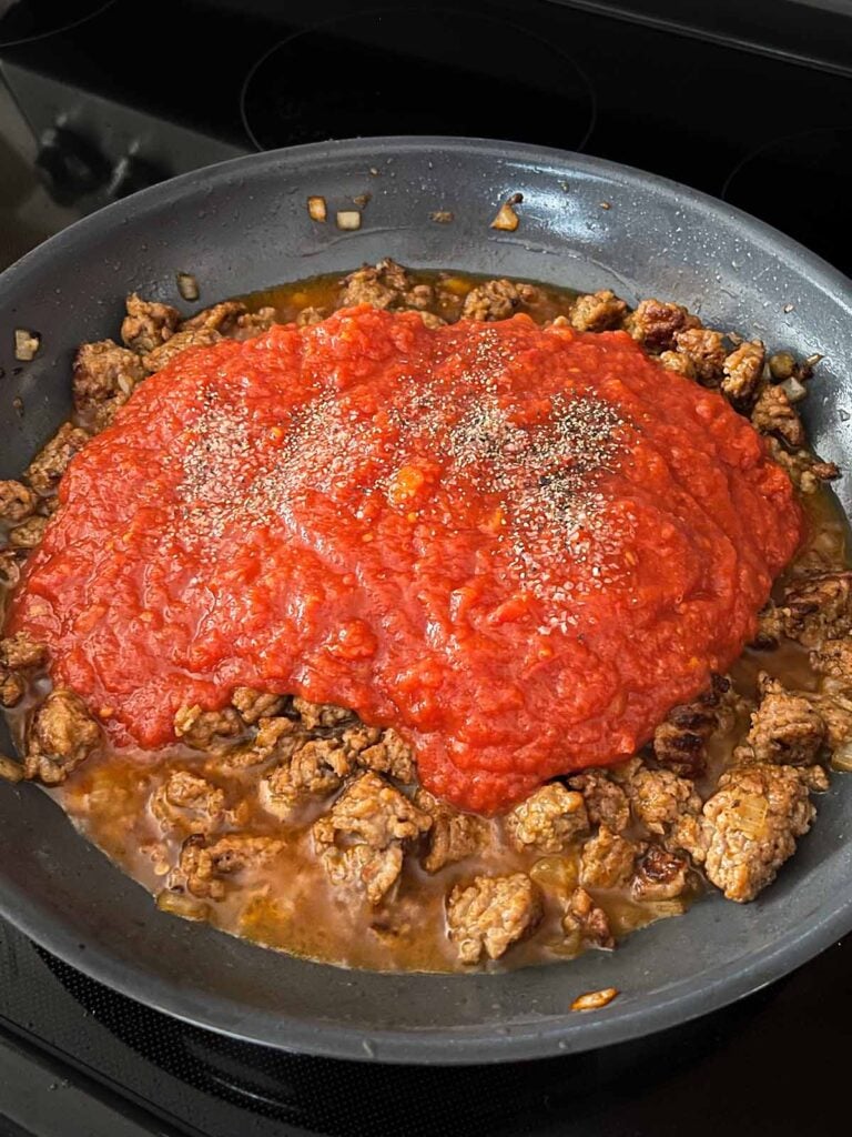 Crushed tomatoes added to italian sausage in a skillet.