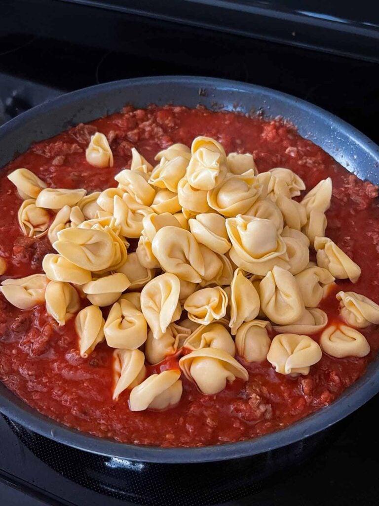 Tortellini added to a tomato sauce in a skillet.