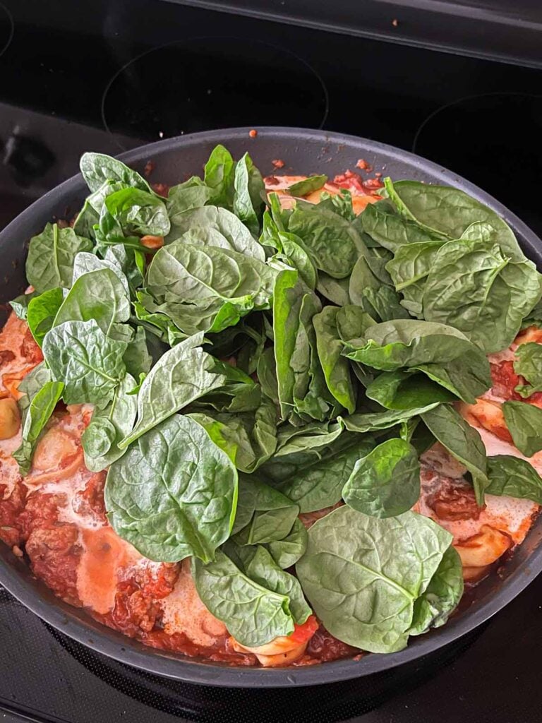 Spinach being added to a tortellini and italian sausage dish.