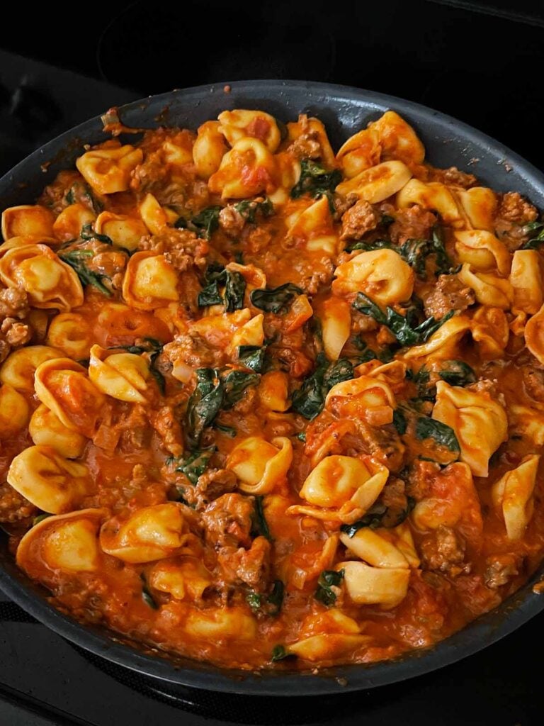 Tortellini with italian sausage and spinach in a skillet.