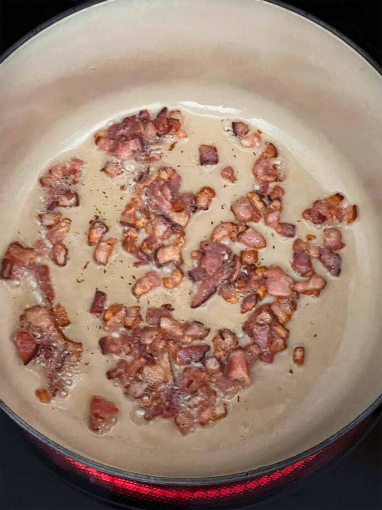 Chopped bacon frying in a dutch oven.