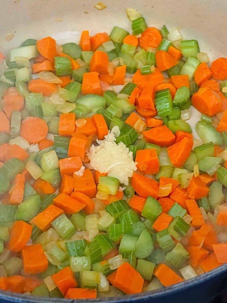 Garlic being added to onions, celery, and carrots in a dutch oven.
