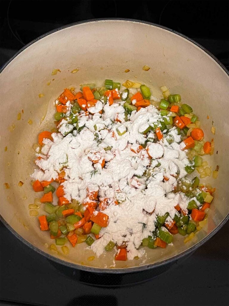 Flour being added to a mirepoix in a dutch oven.