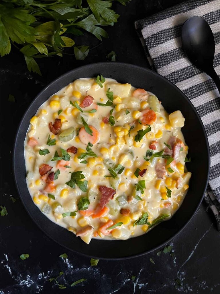 Potato corn chowder in a dark bowl on a dark surface.