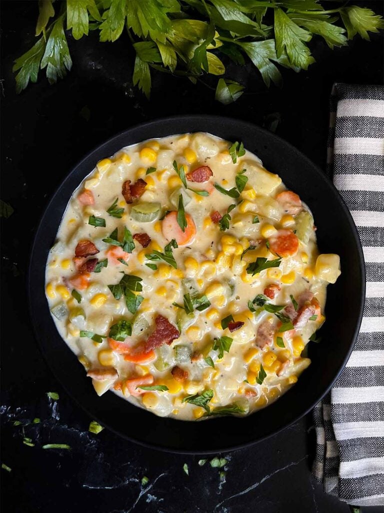 Potato corn chowder in a dark bowl on a dark surface.