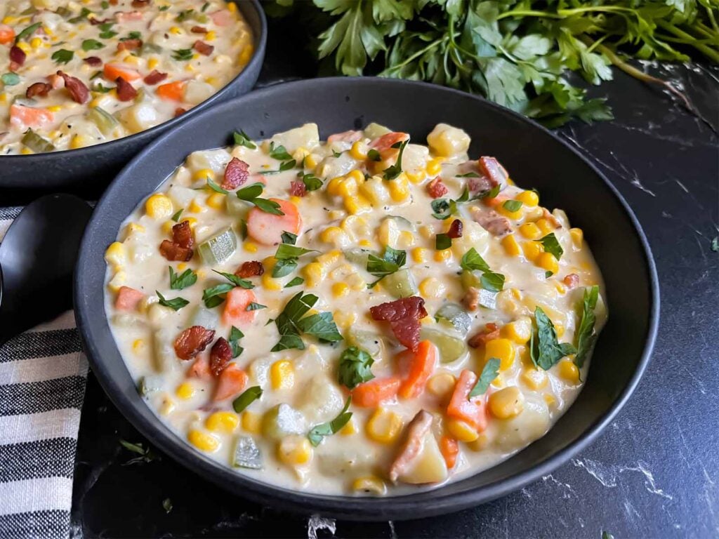 Potato corn chowder in a dark bowl on a dark surface.