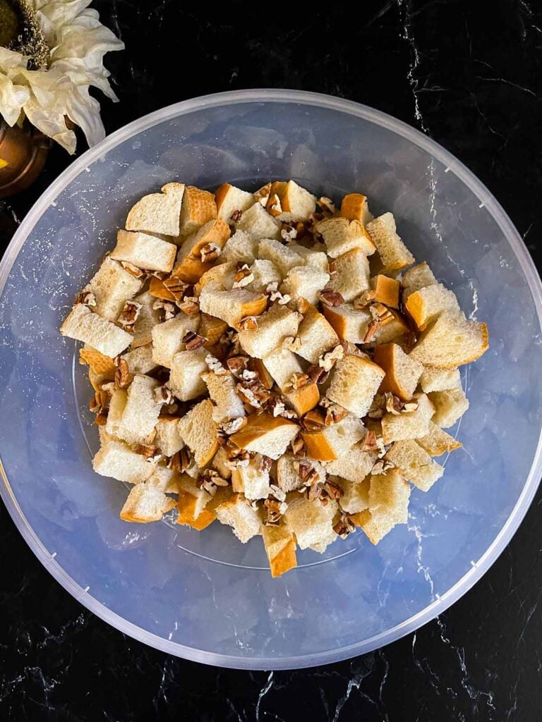 Bread cubes and pecans in a large bowl on a dark surface.