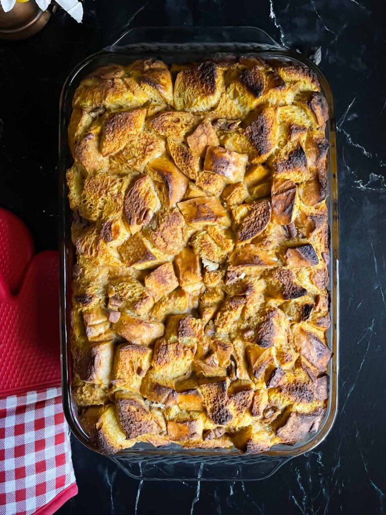 Baked pumpkin bread pudding in a 9x13 baking pan on a dark surface.